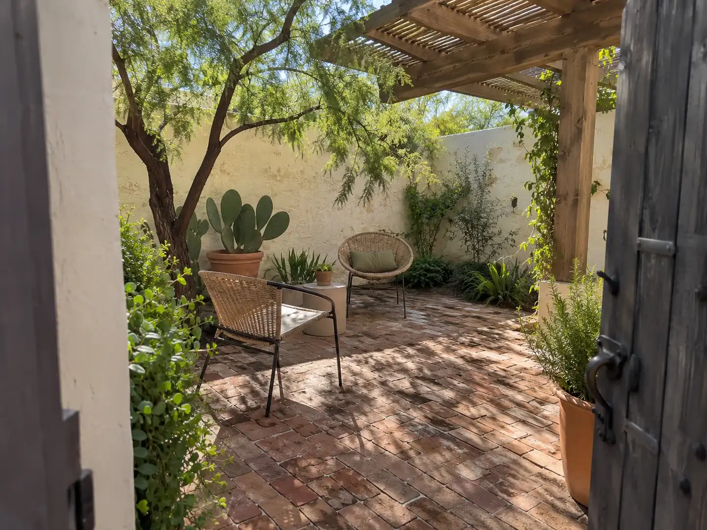 Shaded brick courtyard under a wood pergola with a prickly pear in a planter and two chairs